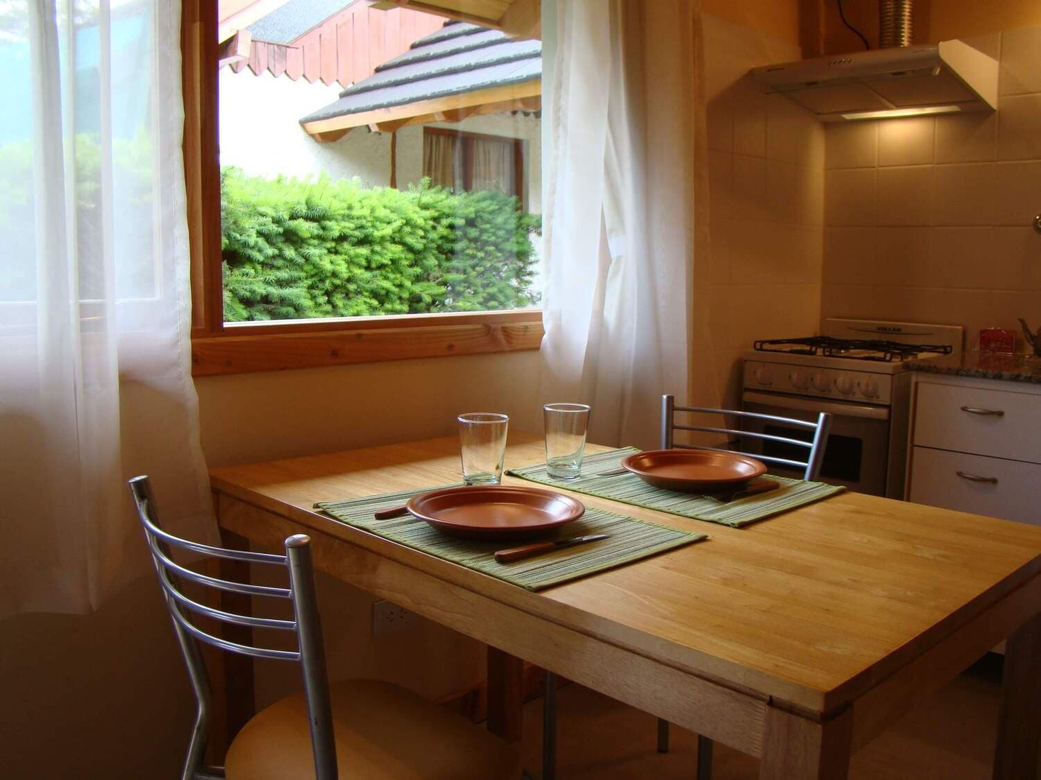 Dining table with plates, glasses, and cutlery, with window view of the monoambiente at Cabañas Denise